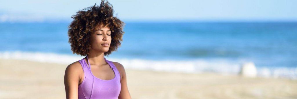 curly hair woman eyes closed meditate on beach in blue sky