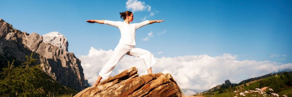 woman stood on rock practicing yoga in blue cloudy sky