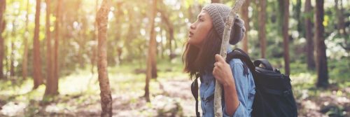young woman holds tree stick hiking in forest