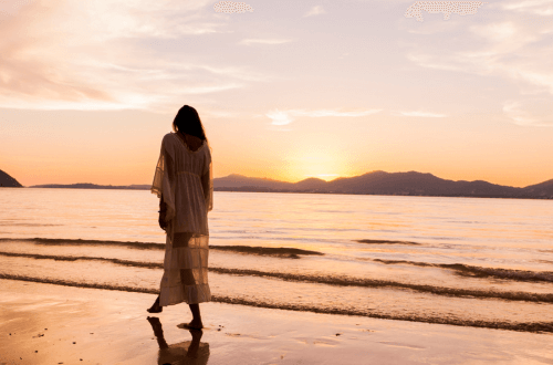 Woman walking along beach in golden sunlight looking for the Wave of Abundance