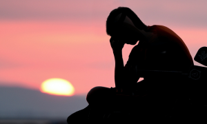 shadow hands on face sits on bench watching sunset red clear sky
