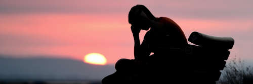 shadow hands on face sits on bench watching sunset red clear sky