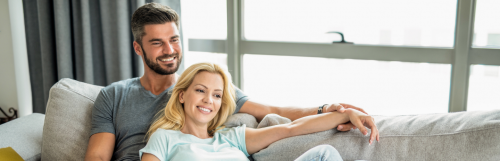 couple sitting on white coach smiling hand in hand in living room