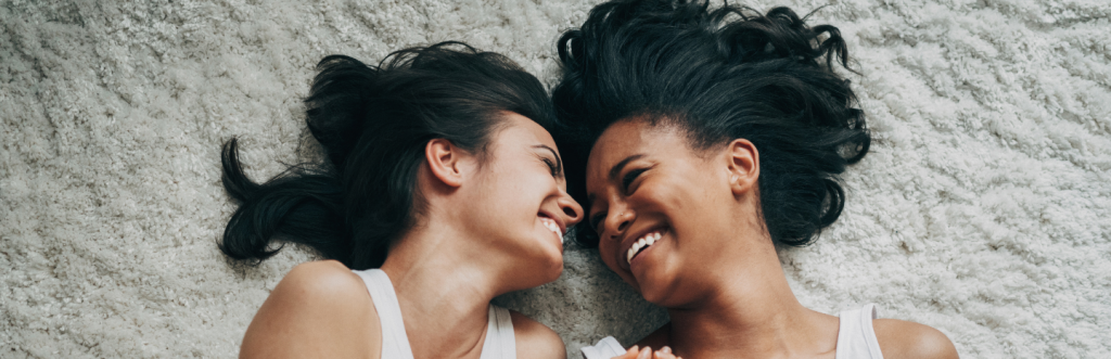 two girls lies on white fluffy carpet smiles at each other