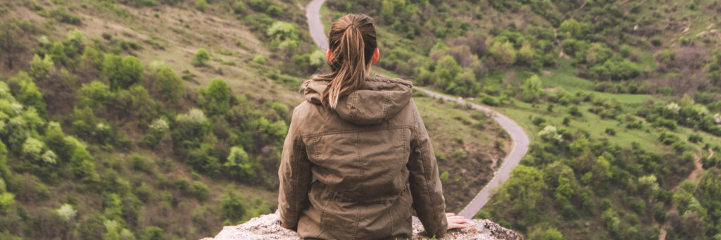woman facing backward stands alone on rock sightseeing